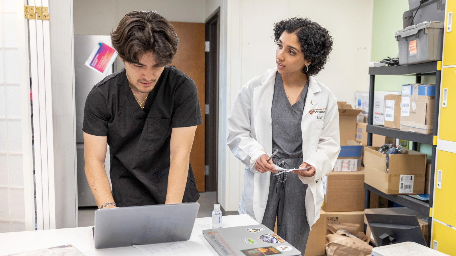 Sonali in a clinic conversing with her medical student peer around a laptop.