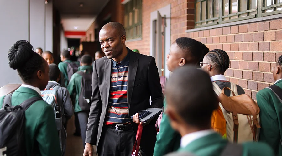 A teacher talks with students in a school hallway.