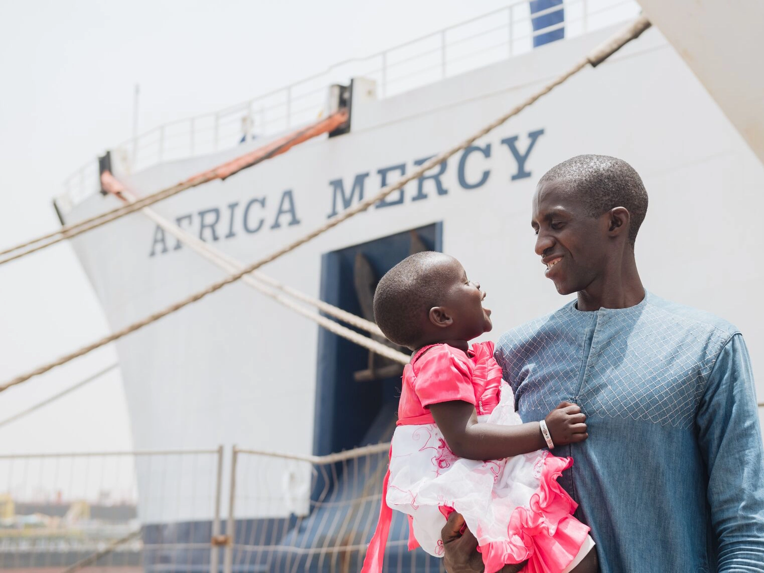 A father holds his child in front of a hospital ship.